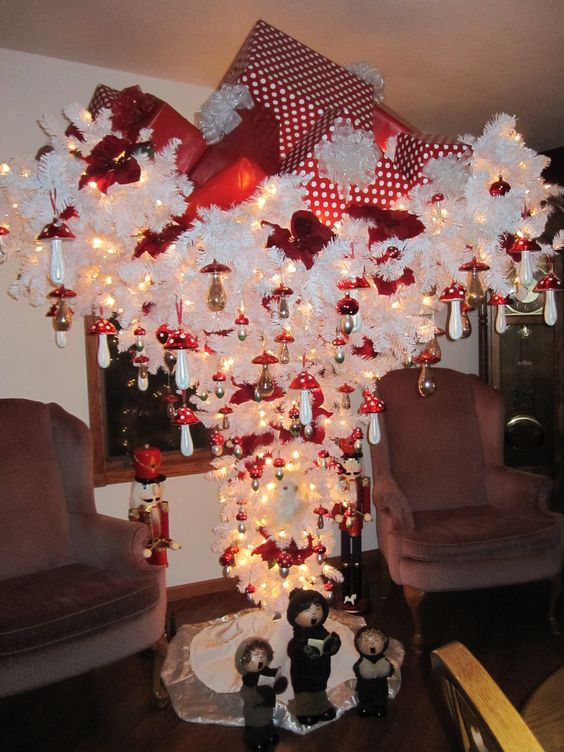 White Christmas tree decorated with red ornaments and large gifts on its head.